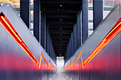 A modern architectural corridor with sleek lines and vibrant red lighting. The perspective creates a sense of depth, leading the eye towards the end of the passage.