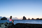 Girl sitting on rocks admiring sunrise at Pointe des Chateaux, Grande-Terre, Guadeloupe, overseas region of France,Leewards Islands, Lesser Antilles, Caribbean