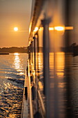 Spiegelung in Fenstern an der Seite des Boutique-Flusskreuzfahrtschiffs MS Thurgau Saxonia (Thurgau Travel) im Peenestrom bei Sonnenaufgang, Wolgast, Mecklenburg-Vorpommern, Deutschland, Europa