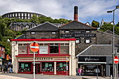 Geschäfte in der Innenstadt mit Oban Distillery und McCaig's Tower (oder McCaig's Folly) dahinter, Oban, Schottland, Argyll and Bute Council, Vereinigtes Königreich, Europa