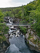  Aerial view of Rogie Falls waterfall on the River Allt an Dubh with man on suspension bridge, near Strathpeffer, Highland Council, Scotland, United Kingdom, Europe 
