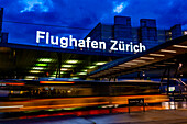 Illuminated Entrance Sign to Zurich Airport and a Bus in Motion at Night in the Airport in Kloten, Zurich, Zurich Canton, Switzerland.