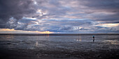  Lonely figure on the reflecting beach at sunset, North Sea, Lower Saxony, Germany 