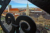 Blick durch das geschwungene Gitter am Turm der Peterskirche auf die Frauenkirche und Neues Rathaus am Marienplatz, München, Bayern, Deutschland