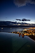Couple relaxes in infinity jacuzzi pool at Arakur Ushuaia Resort and Spa overlooking city lights at dusk, Ushuaia, Tierra del Fuego, Patagonia, Argentina