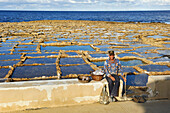 Salt man worker selling salt by the salt pans on the north coast of Gozo Island, Malta, Mediterranean Sea,  Southern Europe