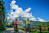  Man and woman mountain biking towards the Gotzenalm, Watzmann mountain in the background, Berchtesgaden National Park, Berchtesgaden Alps, Berchtesgaden, Upper Bavaria, Bavaria, Germany 