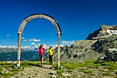 Mann und Frau beim Wandern gehen durch Holzbogen, Campagneda-Pass, Valmalenco, Alta via della Valmalenco, Bernina-Alpen, Lombardei, Italien