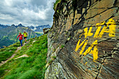 Mann und Frau beim Wandern vor Felswand mit Wegaufschrift, Valmalenco, Alta via della Valmalenco, Bernina-Alpen, Lombardei, Italien