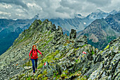 Frau beim Wandern steigt über Felswand auf, Berge im Hintergrund in Wolken, Valmalenco, Alta via della Valmalenco, Bernina-Alpen, Lombardei, Italien