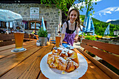  Young woman in a dirndl serving Kaiserschmarrn, Albert-Link-Hütte, Spitzing, Mangfall Mountains, Bavarian Alps, Upper Bavaria, Bavaria, Germany 
