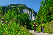  Man and woman mountain biking with a rock face in the background, around the Wendelstein mountain, Mangfall Mountains, Bavarian Alps, Upper Bavaria, Bavaria, Germany 