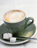 Cappuccino in grüner Tasse mit Löffel & Würfelzucker