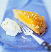 A piece of caramelised mango tart with cream on a plate