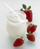 Ein Glas Naturjoghurt mit Löffel, daneben frische Erdbeeren