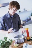 Young man seasoning soup with salt during cooking