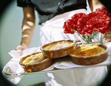 Hands holding tray with Crema catalana and carnations