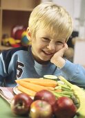 Small boy sitting at table with fruit and vegetables