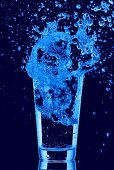 Blaues Wasser spritzt aus Wasserglas