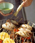 Calamari kebabs on the barbecue being brushed with oil