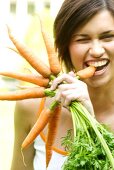 Woman with a bunch of carrots, biting into one of them
