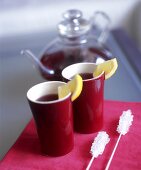 Two beakers of fruit tea with lemon wedges, sugar sticks