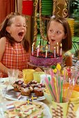 Zwei Mädchen pusten Kerzen auf Geburtstagstorte aus