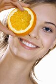 Young woman holding a slice of orange in front of her eye