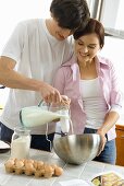 Young couple baking a cake, with hand blender and milk jug