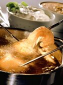 Shrimps in batter on fondue forks in boiling oil