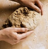 Preparing mixed-grain bread: hands forming oblong loaf