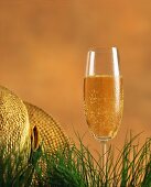 A champagne glass in the grass beside a straw hat