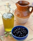 Olivenöl, eine Schale schwarze Oliven und ein Tonkrug
