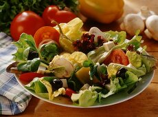 Mixed salad leaves on a plate with vegetables behind