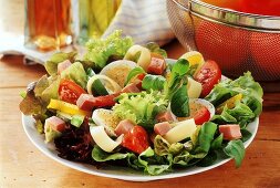 Blattsalat mit Schinken auf Teller; Essig und Öl; Tomaten