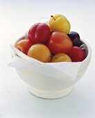 Plums of various colours in white bowl