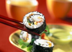 Maki sushi on chopsticks over a plate