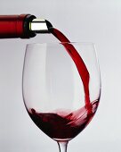 Rotwein aus Flasche mit Silberfolie in ein Glas gießen