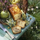 Olive and ham loaf, apples & herbs in basket in meadow