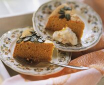 Two pieces of pumpkin cake with pumpkin seeds, one with cream