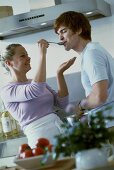 Young couple in kitchen tasting soup from spoon