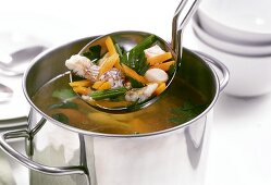 Fish soup with vegetables in pot and ladle