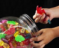 Children's hands taking fruit gum out of glass container
