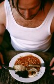 Man in vest eating beans with sausage and fried egg