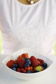 Assorted berries in white bowl, woman in background