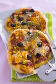 Two vegetable pizzas with sweetcorn and cheese, pizza cutter