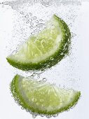 Lime wedges falling into mineral water