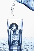 Pouring mineral water into a glass containing ice cubes