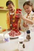 Two girls pouring ketchup onto minced meat
