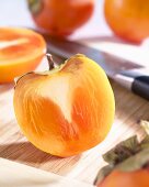 Halved persimmon on chopping board with knife